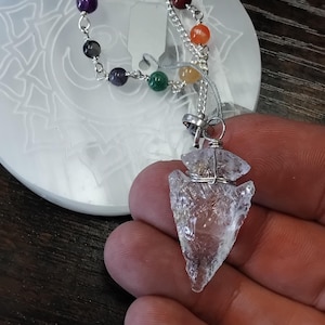 Pode incluir: Um pingente de cristal de quartzo transparente com uma corrente de prata e sete contas de chakra. As contas são roxas, pretas, azuis, verdes, amarelas, laranjas e vermelhas.