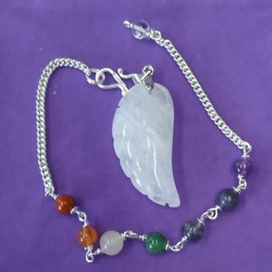 Op de afbeelding: Een zilveren ketting met een witte kristallen vleugel hanger en zeven gekleurde kralen. De kralen zijn rood, oranje, wit, groen, grijs, donkergrijs en paars.
