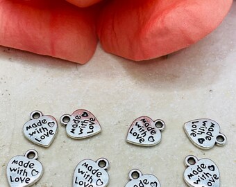 Puede incluir: Ocho encantos de corazón plateados con el texto "Made with Love" en cada encanto.
