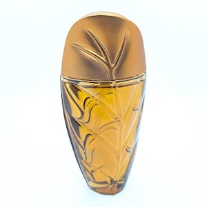 Könnte beinhalten: Ein Parfümflakon mit einem blattartigen Design. Die Flasche hat eine hellbernsteinfarbene Farbe mit einem goldfarbenen Deckel. Das Glas hat ein in die Oberfläche geätztes Blättermuster. Der Deckel hat ein Blattdesign.