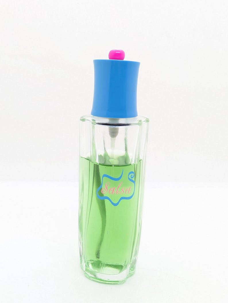 May include: A clear glass perfume bottle filled with green liquid. The bottle has a blue cap with a pink top. The word "Salsa" is written on the bottle in a light blue script.