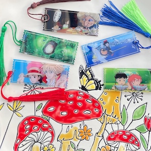 May include: Five colourful bookmarks featuring different images from the Studio Ghibli film, Spirited Away. Each bookmark has a tassel attached. The bookmarks are on a white background with a painted floral design.