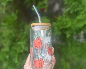 May include: A clear glass reusable water bottle with a bamboo lid and a straw. The bottle has a pattern of orange pumpkins with green stems and leaves.