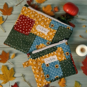 May include: Two patchwork zipper pouches with a floral and geometric design. The pouches feature a mix of colors including green, yellow, red, and blue. The pouches are decorated with the text "Zuy Boutique".