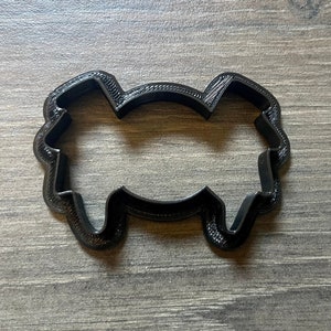 May include: Black plastic cookie cutter in the shape of a cloud with a wavy bottom. The cookie cutter is on a wooden surface.