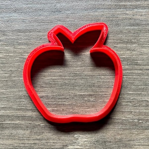 May include: A red plastic apple-shaped cookie cutter.