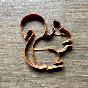May include: A brown plastic cookie cutter shaped like a squirrel. The cutter has a detailed design with a bushy tail and a defined head.
