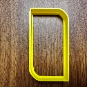May include: A yellow plastic cookie cutter shaped like a rectangle with rounded corners.