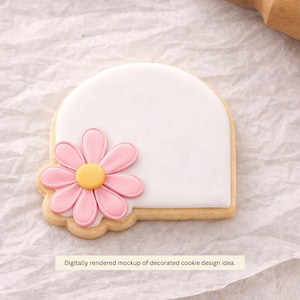 May include: A decorated cookie with a white icing background and a pink flower design. The flower has a yellow center. The cookie is on a white surface. The text on the image says "Digitally rendered mockup of decorated cookie design idea."