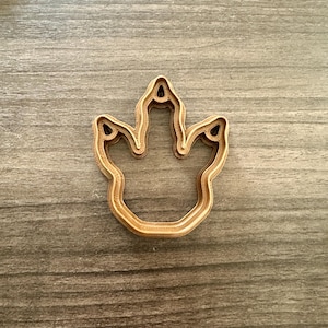 May include: A light brown dinosaur footprint cookie cutter. The cutter is made of a light brown material and has a three-toed design. The footprint is a classic shape, perfect for making dinosaur-themed cookies or treats.