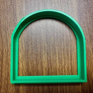 May include: A green plastic cookie cutter shaped like an arched window.