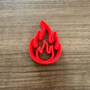 May include: A bright red flame-shaped cookie cutter. The cutter is made of plastic and has a detailed design. The flame shape is a popular design for baking and crafting projects.