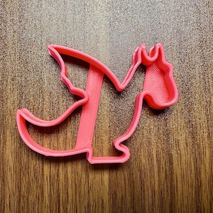 May include: Pink plastic cookie cutter shaped like a dragon with wings and a tail.