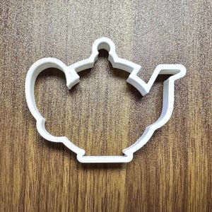May include: White plastic cookie cutter shaped like a teapot.