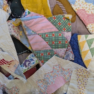 Op de afbeelding: Een verzameling stoffenresten in verschillende kleuren en patronen, waaronder roze, blauw, groen en wit. De resten zijn in een willekeurig patroon gerangschikt, waardoor een patchwork-effect ontstaat.