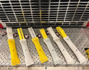 Pode incluir: Seis brinquedos de puxar retangulares de tecido dispostos em fila, numerados de um a seis. Cada brinquedo apresenta uma combinação de material tecido branco e amarelo com costuras e uma alça em laço no topo, com padrões variados.