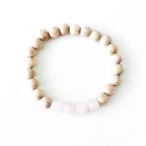 Könnte beinhalten: Ein Armband aus Holzperlen mit einer Reihe hellrosa Perlen in der Mitte.