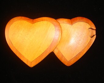 May include: Two interlocking wooden heart-shaped boxes, one light brown and the other a darker shade of brown.