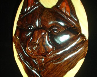May include: A wooden puzzle box with a carved image of a dog's head. The dog is brown and black and has a serious expression. The box is oval shaped and has a light wood background.