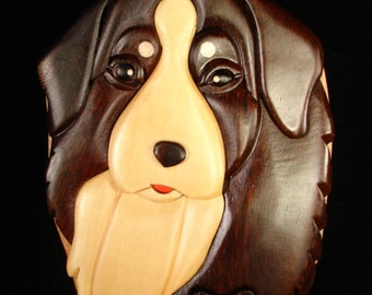 May include: A wooden puzzle box shaped like a Bernese Mountain Dog's head. The box is made of dark brown and light wood and has a detailed carving of the dog's face.