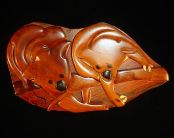 May include: A wooden puzzle box with two carved koalas on a branch. The box is made of dark wood with a natural finish. The koalas are intricately carved and have black eyes.