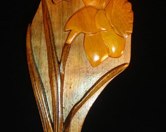 May include: A wooden puzzle box shaped like a daffodil flower. The box is made of light brown wood with a dark brown stain. The flower is carved in detail and has a yellow colour.