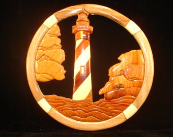 Könnte beinhalten: Ein Wandkunstwerk aus Holz, das einen Leuchtturm mit roten und weißen Streifen zeigt, umgeben von Wellen und felsigen Klippen. Der Leuchtturm ist aus verschiedenen Holzarten geschnitzt, was ein einzigartiges und filigranes Design ergibt.