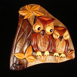 May include: A wooden owl puzzle box with two owls carved into the wood. The owls are brown and have large eyes. The box is shaped like a triangle and has a leaf design on the top.