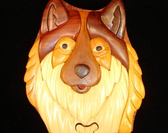 May include: A wooden puzzle box shaped like a dog's head. The dog has brown, black, and white fur. The puzzle box is made of multiple pieces of wood that fit together.