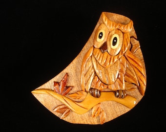 Op de afbeelding: Een houten uil puzzeldoos met ingewikkelde details. De uil zit op een tak met bladeren die in het hout zijn gegraveerd. De doos is gemaakt van lichtbruin hout met een natuurlijke afwerking.