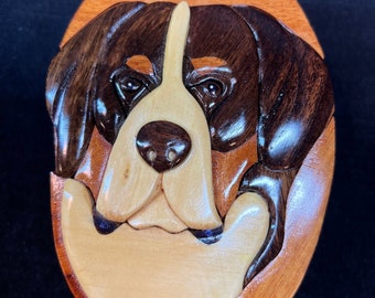 May include: A wooden puzzle box with a carved image of a Bernese Mountain Dog's face. The dog's fur is depicted in shades of brown, black, and white.