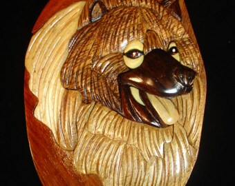 May include: A wooden puzzle box with a carved image of a dog's head. The dog has brown fur, a black nose, and a long tongue sticking out. The box is made of different types of wood, creating a unique and intricate design.