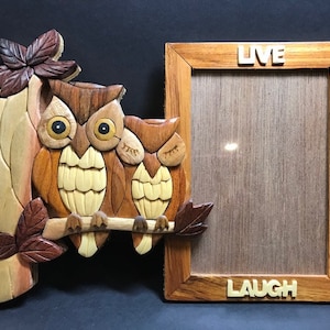 May include: A wooden picture frame with two carved owls on a branch. The frame has the words "LIVE", "LOVE", and "LAUGH" on it.