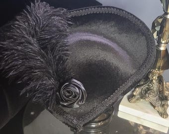 May include: A black velvet hat with a wide brim, a black feather, and a black rose accent.