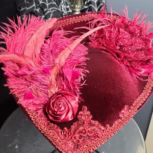 May include: A burgundy velvet hat with a pink rose, pink feathers, and a pink sequined trim.