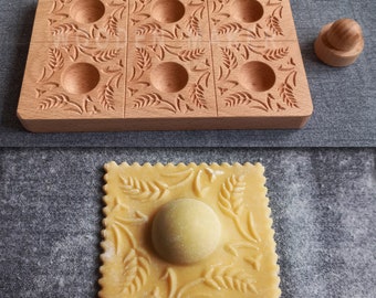 May include: A wooden ravioli mold with a wheat design and 12 individual molds. The mold is used to create decorative ravioli with a wheat design. A single ravioli is shown in the bottom of the image, with a wheat design and a round filling.