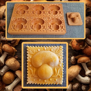 Op de afbeelding: Een houten ravioli-mal met zes paddenstoelvormige holtes en een enkele paddenstoelvormige stempel. Er wordt ook een enkele ravioli met een paddenstoelontwerp getoond. De mal en stempel zijn gemaakt van lichtbruin hout.