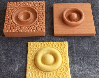 May include: Three wooden squares with a raised circular design in the center. The squares are in different shades of brown and yellow. The design is a circle with a smaller circle in the center.