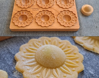 May include: A wooden mold with six flower-shaped designs for making cookies or pastries. The mold is made of light brown wood and has the text "Wooden Maker" printed on it. A close-up of a cookie made with the mold shows a detailed flower design.