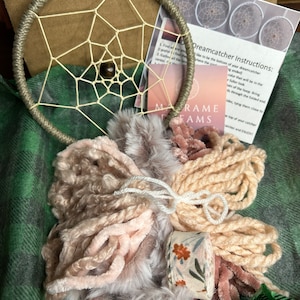 May include: A dreamcatcher kit with a beige hoop, white string, beige and pink yarn, a white feather boa, and a beige ribbon with a floral pattern. The kit includes instructions for making a dreamcatcher.