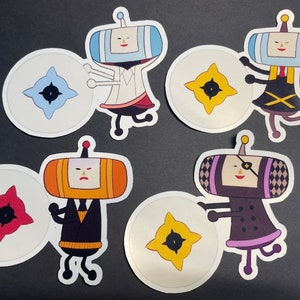 May include: A collection of colorful stickers featuring cartoon characters with rectangular heads and round, star-shaped designs. The characters are in various outfits, holding the star-shaped designs. The stickers are on a black surface.