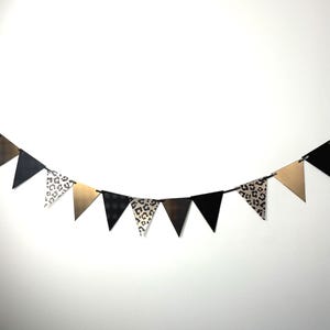 May include: A decorative banner featuring triangular flags in black, gold, and leopard print. The flags are strung on a black cord, creating a festive decoration. Suitable for parties and celebrations. The banner is a stylish decoration.