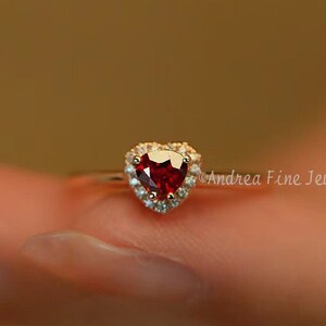 Peut inclure: Une bague en or avec une pierre rouge en forme de cœur entourée de petites pierres blanches.