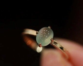 May include: A delicate gold ring with a light green oval gemstone set in a prong setting.