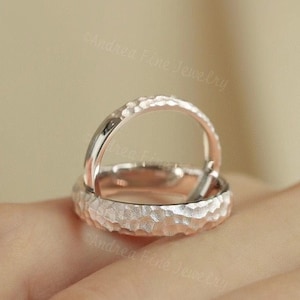 Può includere: Due fedi nuziali in argento martellate, una leggermente più grande dell'altra, sono impilate l'una sull'altra. Le fedi sono lisce e hanno una finitura opaca.