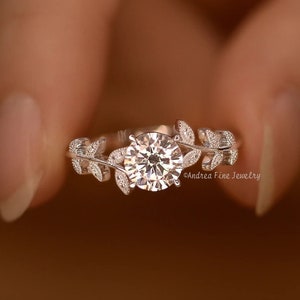 Może przedstawiać: Srebrny pierścionek z dużym, okrągłym, przezroczystym kamieniem osadzonym w środku. Obrączka jest ozdobiona delikatnymi wzorami liści.