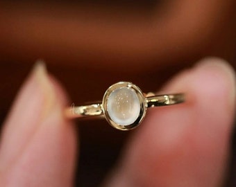 May include: A gold ring with a white moonstone set in a bezel setting.