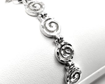May include: A silver bracelet with a repeating pattern of spiral circles. The bracelet is on a white surface.