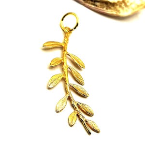 May include: A gold-colored pendant charm in the shape of a branch with leaves. The charm is made of metal and has a loop at the top for attaching to a necklace or bracelet.