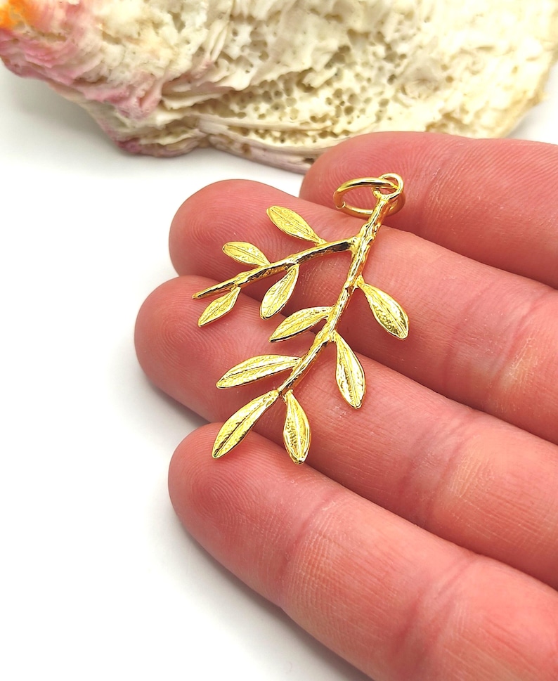 May include: Gold-toned olive branch pendant charm with a textured finish. The charm has a loop at the top for attaching to a necklace or bracelet.